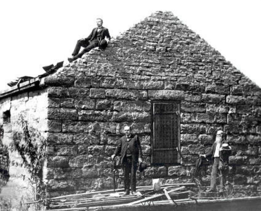 The jail at Liberty in 1888, half in ruins. Andrew Jenson sits on the roof; Edward Stevenson and Joseph S. Black stand beside it.